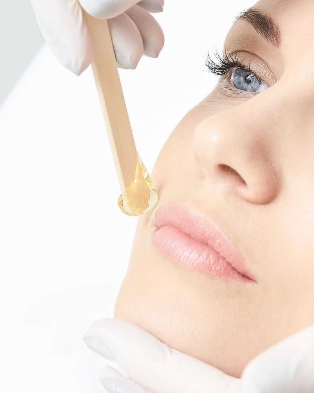 Facial waxing in progress, close-up of woman's face with stick applying wax.