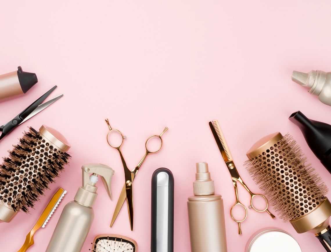 Hair styling tools and products on a pink background.