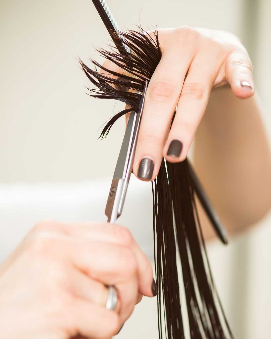 Hair being trimmed by scissors held by hands with black nail polish.